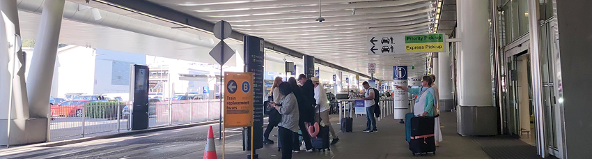 Sydney Domestic Airport terminal kerbside with Priority Pick-Up and Express Pick-Up signs and arriving passengers with luggage