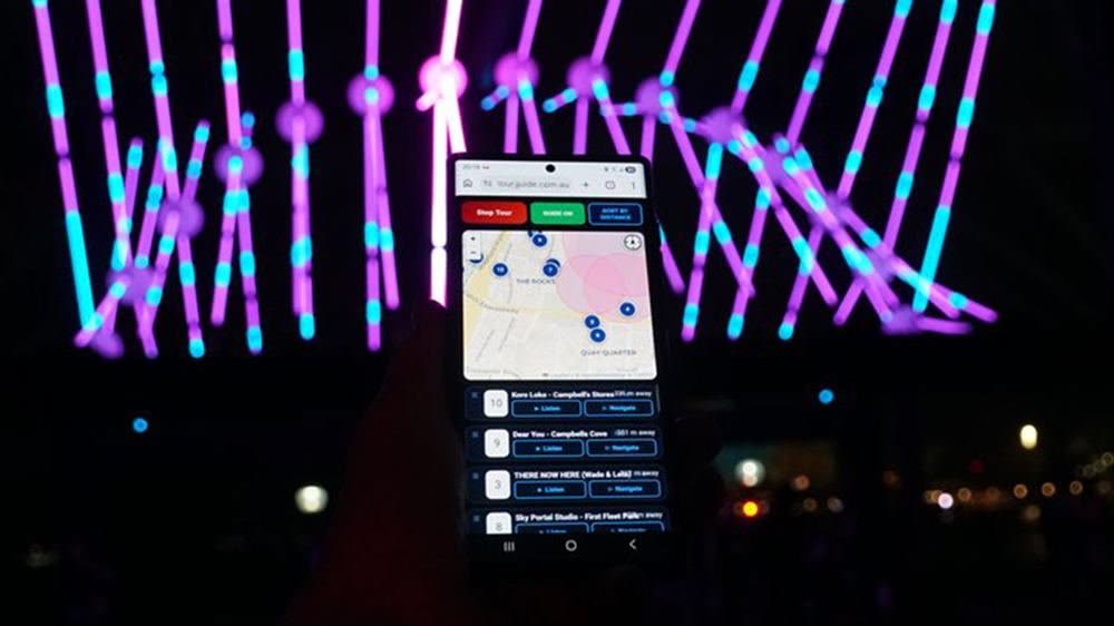 Phone running the free light festival audio guide in front of an illuminated light installation at night