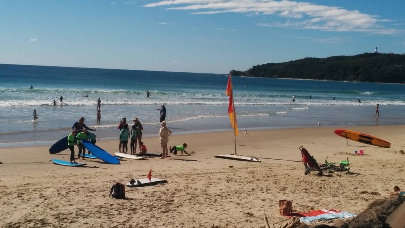 Byron Bay main beach with surf school and the Cape Byron lighthouse on the headland